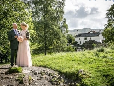 Mature Wedding Couple standing in Flower Meadow at Rydal Water after eloping to the Lake District