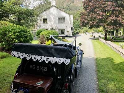 Just Married garland hangs on the back of a vintage Austin 7 as it waits to take the Bride and Groom on their way at Cote How in the Lake District