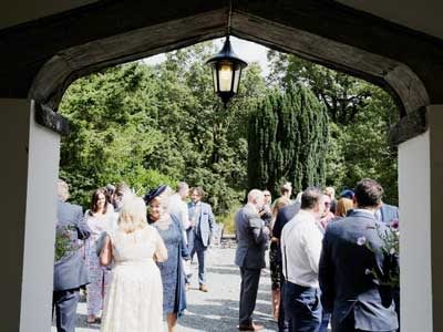 Looking through the tudor porch at Cote How -The welcome drinks reception on the terrace at Cote How as new guests arrive for the humanist wedding on the lawn