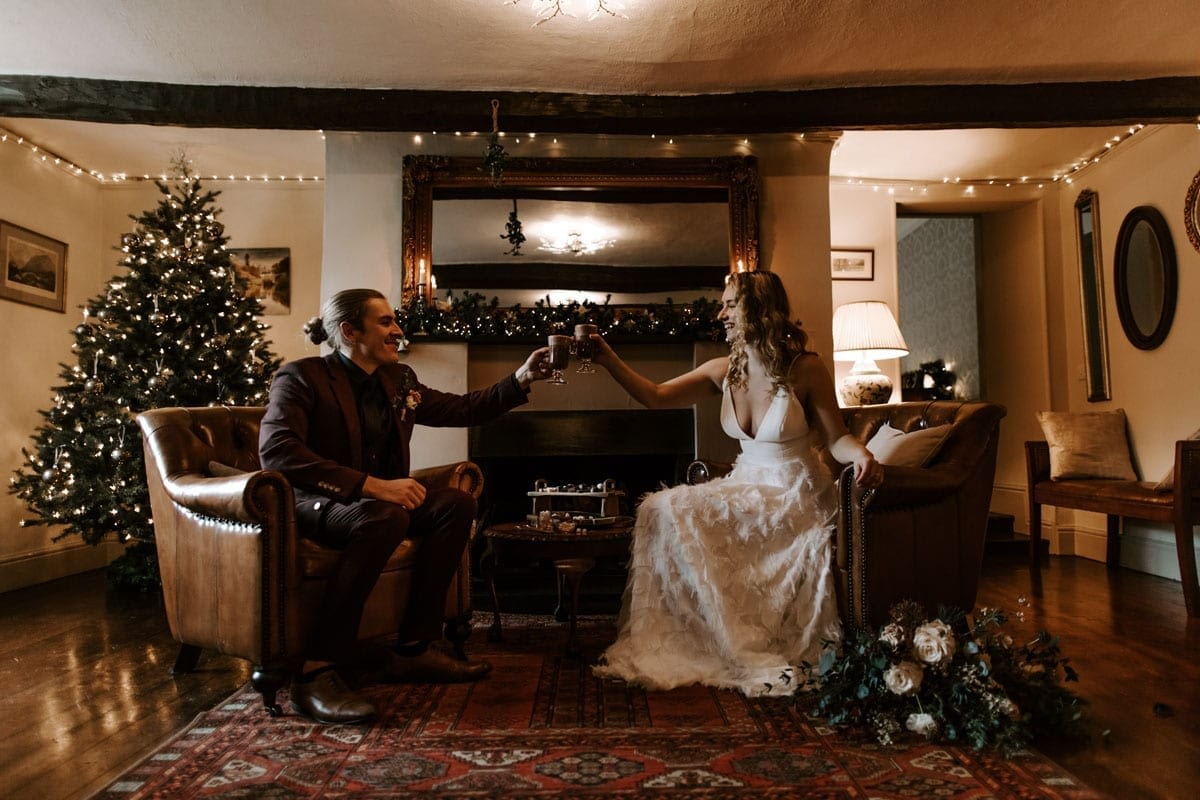 Couple-Celebrating-with-Hot-Chocolate-by-the-Log-Fire-and-Christmas-Tree