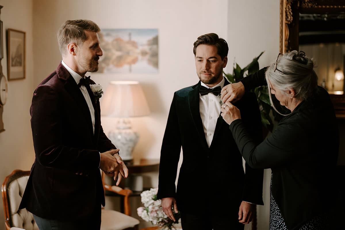Two Grooms having their buttonholes attached before the wedding ceremony