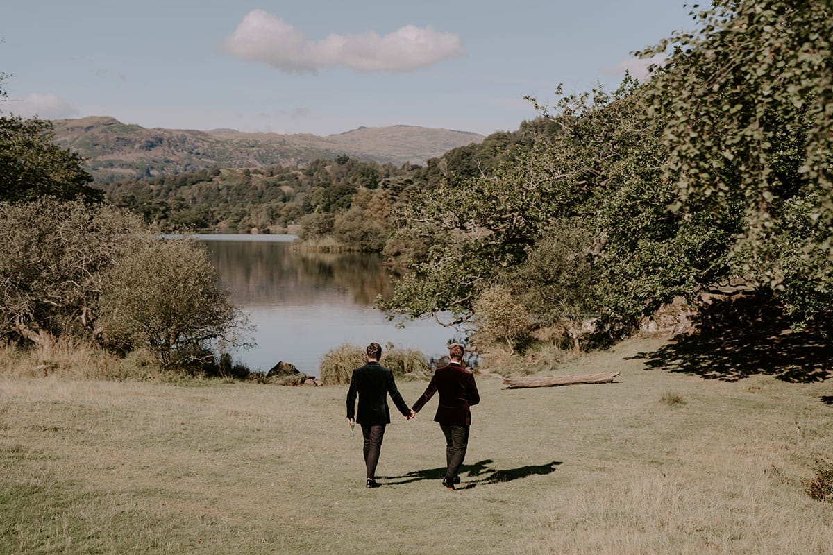 Gay wedding couple walking down to Rydal water from lakeside venue