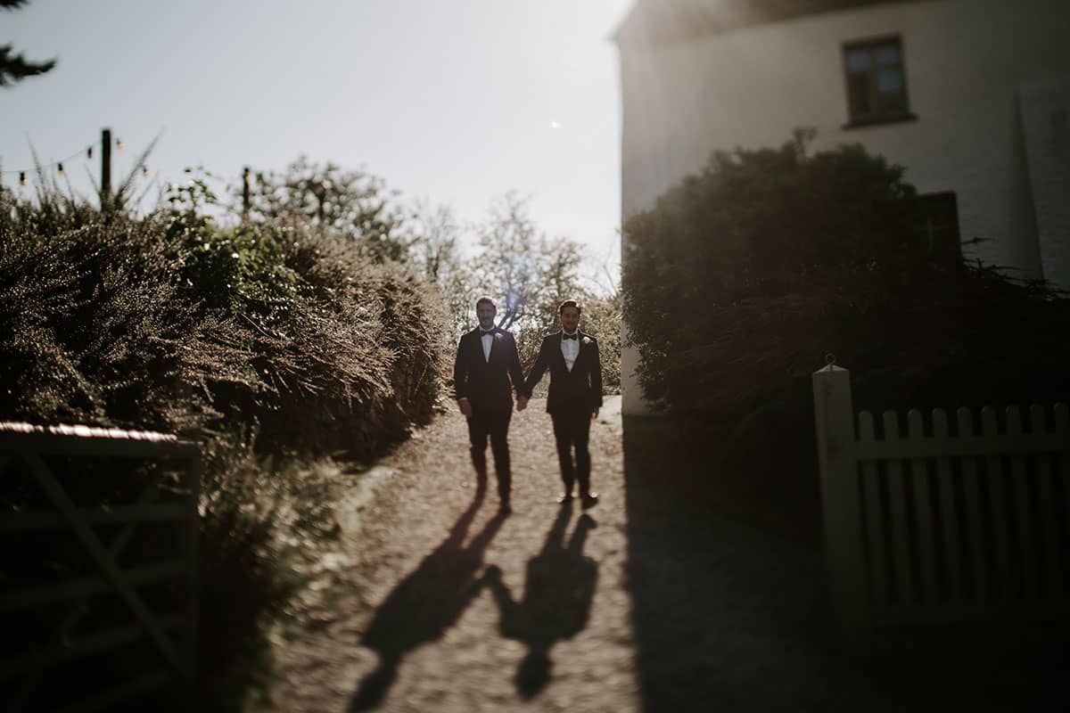 Two grooms walking down to the barn from the house for their ceremony