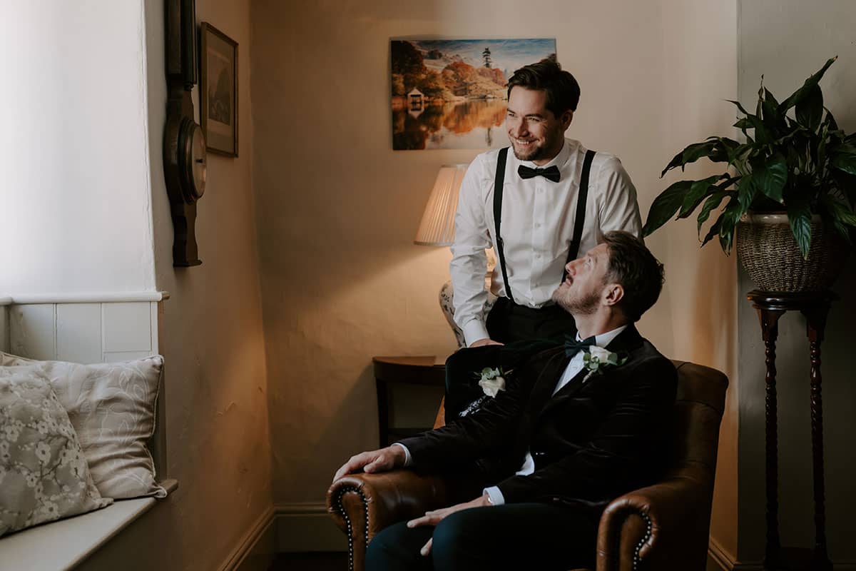 Gay wedding couple relaxing in leather armchair in the house before elopement ceremony